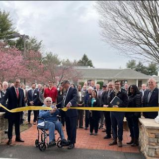 A community gathering for a ribbon-cutting ceremony, marking the opening of a new facility amidst blooming trees.