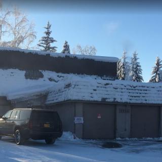 A snow-covered building with a car parked outside on a sunny winter day.