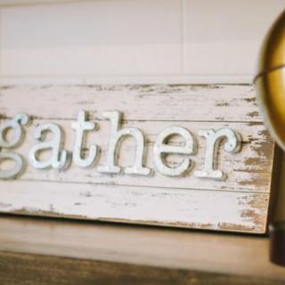A rustic wooden sign featuring the word 'gather'.