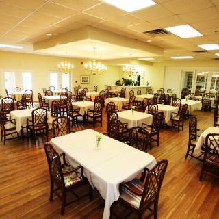 A spacious dining room with neatly arranged tables and chairs, illuminated by elegant chandeliers.
