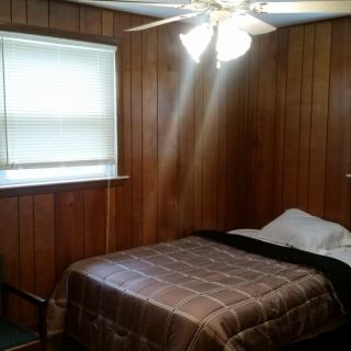 A cozy bedroom with wood paneling and a ceiling fan.
