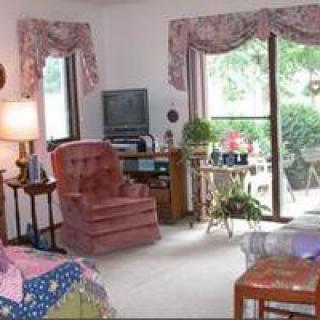 A cozy living room with a pink armchair, television, and large window offering a garden view.