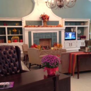 A cozy living room with a fireplace, television, and bookshelves decorated with flowers and fall-themed accents.