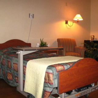 A hospital room with a bed, bedside table, and a comfortable chair under soft lighting.