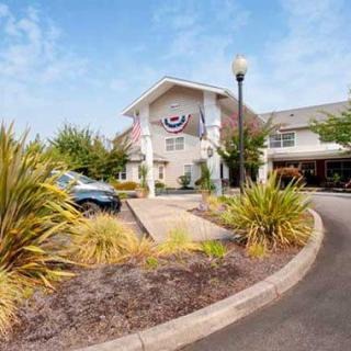 The entrance of a hotel with neatly landscaped surroundings and a parking area during the day.