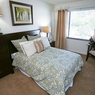 A cozy bedroom with a neatly made bed, bedside lamps, and a large window providing natural light.