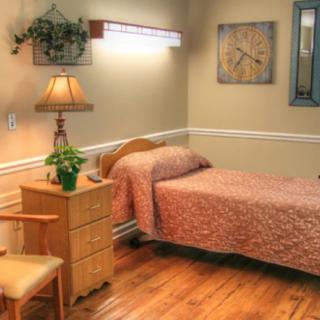 A cozy bedroom with a single bed, wooden flooring, and a bedside lamp.