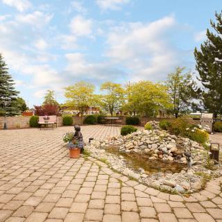 A serene courtyard with a stone pathway, surrounded by trees and a decorative pond under a partly cloudy sky.