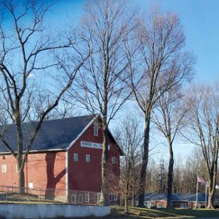 A picturesque red barn surrounded by leafless trees under a clear blue sky.