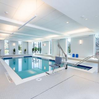 A modern indoor swimming pool with ample natural light, featuring plants and a seating area.