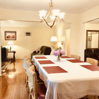 A warm and inviting dining room featuring a long table set with a white tablecloth, surrounded by chairs and illuminated by an elegant chandelier.