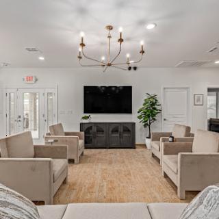 A modern and cozy living room featuring comfortable seating, a chandelier, and a large television.