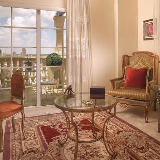 A classic living room with elegant furnishings, featuring a glass table and armchair, overlooking a balcony.