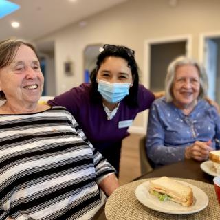 A group of three people enjoying a meal together and smiling indoors.