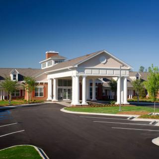 A modern building with a grand entrance featuring large columns and a landscaped driveway.