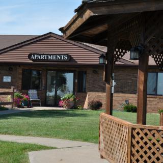 A view of an apartment building entrance with a gazebo and well-kept lawn.