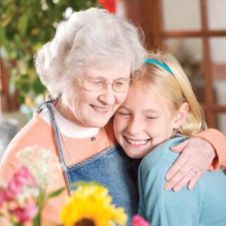 A grandmother and granddaughter share a warm embrace surrounded by flowers.
