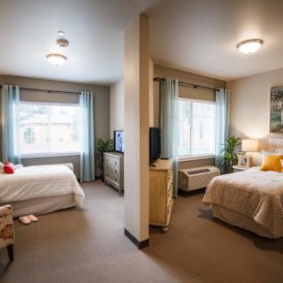 A cozy bedroom with two beds, separated by a partial wall, featuring warm lighting and inviting decor.