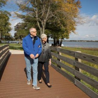 An elderly couple enjoys a pleasant walk along the lakeside on a sunny autumn day.