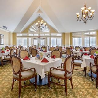 An elegantly set dining room with multiple tables and chairs, featuring chandeliers and a bright, inviting interior.