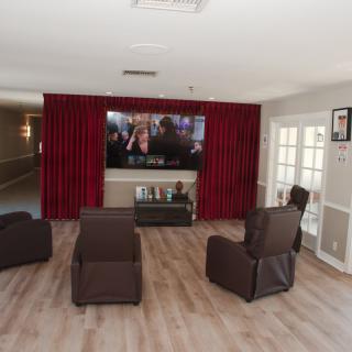A cozy home theater setup with comfortable recliners facing a large television, enhanced by red curtains and a wooden floor.