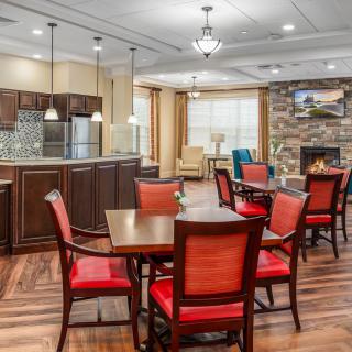 A modern kitchen and dining area with red chairs, wood flooring, and a cozy fireplace.