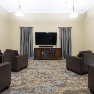 A cozy living room setup with multiple comfortable chairs, a large television, and curtains framing the windows.