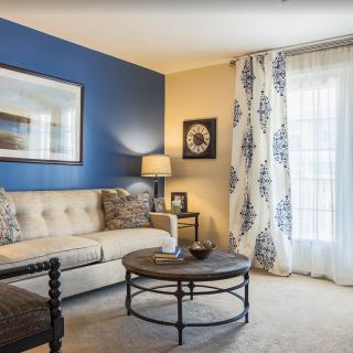 A cozy living room with a beige sofa, circular coffee table, and a blue accent wall.