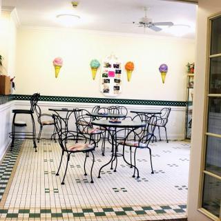 A quaint ice cream parlor with elegantly designed tables and chairs, featuring colorful ice cream cone decorations on the walls.