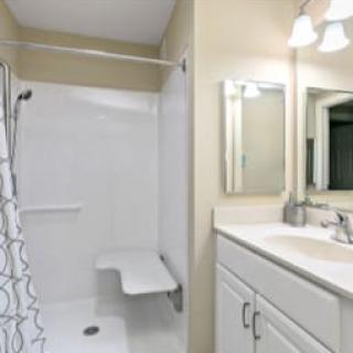 A modern bathroom featuring a white tiled shower with a seat, a vanity with a sink, and a mirror under bright lighting.