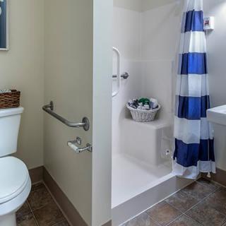 An accessible bathroom featuring a toilet with grab bars and a shower with a blue and white striped curtain.