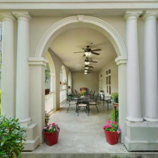 A classic porch with columns and archway, featuring outdoor seating and potted plants.