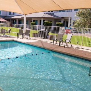 An outdoor swimming pool area with shaded seating and a surrounding fence.