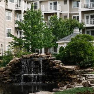 A tranquil waterfall feature in front of an apartment building surrounded by lush greenery.