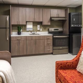 A modern kitchen interior with sleek cabinetry and appliances, featuring a cozy red armchair.
