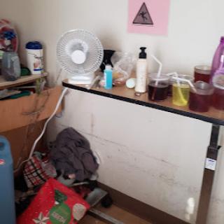 A cluttered workspace filled with various items including bottles, a fan, and some bags.