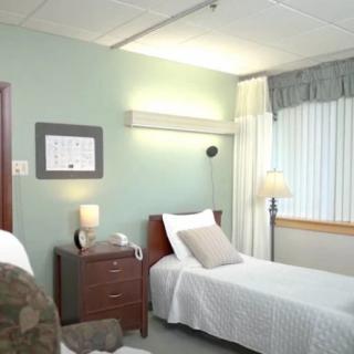 A clean and well-lit hospital room with a neatly made bed and modern furnishings.