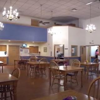 An empty dining room with wooden tables and chairs, illuminated by chandeliers.