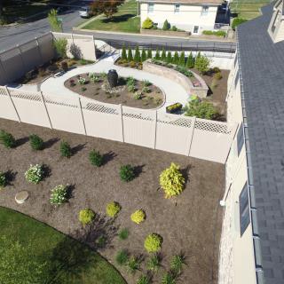 Aerial view of a landscaped garden with a pathway and shrubs surrounded by a fence.