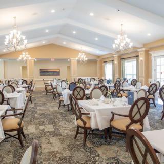 An elegant dining room with neatly arranged tables and chairs, featuring chandeliers and large windows.