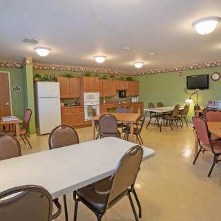 A community room featuring a kitchen area with tables and chairs, equipped with a refrigerator, microwave, and television.