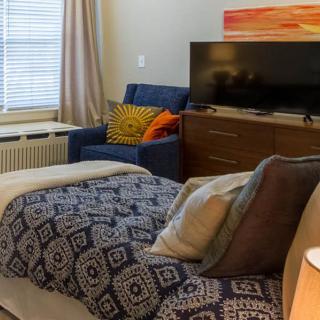 A cozy bedroom with stylish decor, featuring a bed, chair, and television.