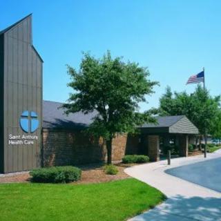 Exterior view of a health care clinic with surrounding trees and an American flag in the background.