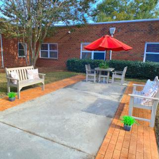 A serene outdoor patio area featuring comfortable benches, a dining table with a red umbrella, and well-maintained landscaping.