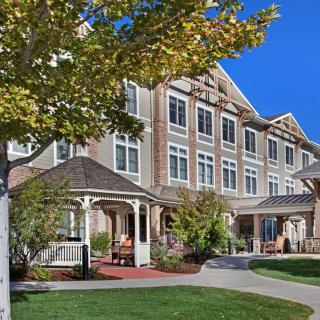 A picturesque residential building surrounded by a well-maintained landscape and trees under a clear blue sky.
