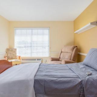 A minimalist bedroom with a large bed, chairs, and a window allowing natural light.