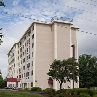 A multi-story hotel building with trees in the foreground under a partly cloudy sky.