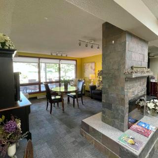 A modern living room with a connected dining area, featuring a stone fireplace and large windows providing ample natural light.