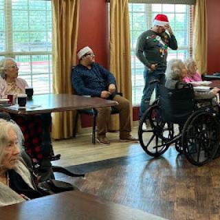 Seniors enjoying a holiday gathering in their activity room, wearing festive red hats.