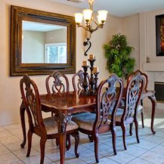 A well-furnished dining room with a wooden table and six chairs, complemented by a large mirror and chandelier.